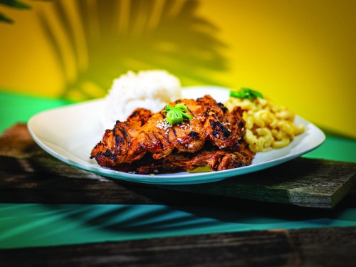 A plate of grilled chicken with rice and macaroni, garnished with green onions, set against a colorful background.