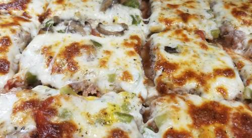 Close-up of cheesy, golden-brown pizza slices topped with vegetables and meat, freshly baked and delicious.