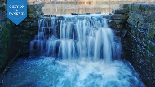 A serene waterfall cascading over stone steps into a calm blue pool, surrounded by nature.