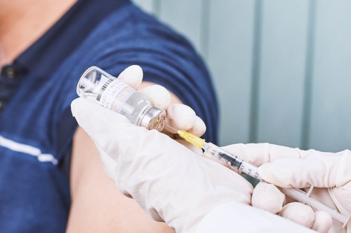 A healthcare professional prepares a syringe with a vaccine while a patient’s arm is visible in the background.