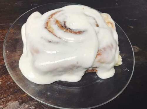 A delicious cinnamon roll topped with creamy white icing on a clear plate.