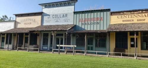 Historic storefronts with colorful facades, including a saloon and barber shop, set against a clear blue sky.