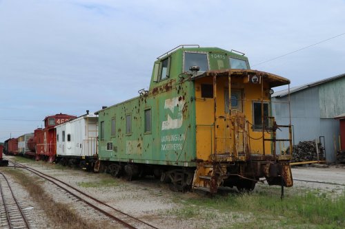 A green and yellow caboose from Burlington Northern, parked alongside other train cars in a rail yard.