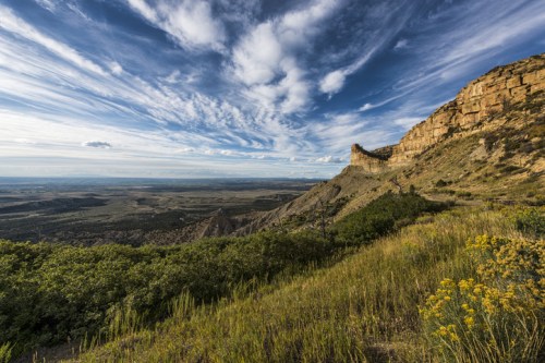 A scenic landscape featuring rolling hills, a rocky cliff, and a dramatic sky with clouds over a lush green valley.