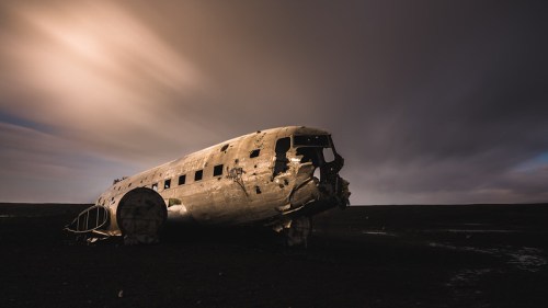 A weathered airplane wreck sits on a barren landscape under a dramatic sky.