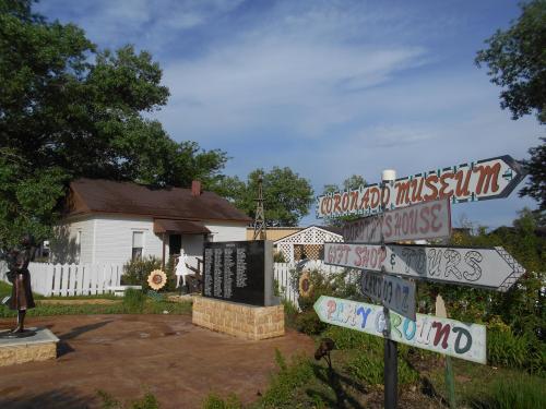 A museum with directional signs, a statue, and a white picket fence surrounded by trees and flowers.