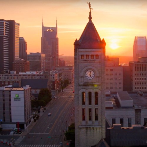 Sunset over a city skyline featuring a clock tower, with modern buildings and a clear sky in the background.