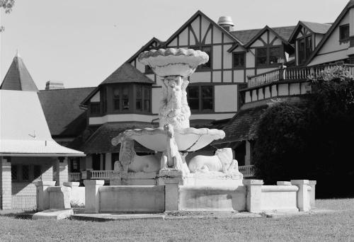 A vintage fountain featuring a lion sculpture, set against a backdrop of a large, ornate building.