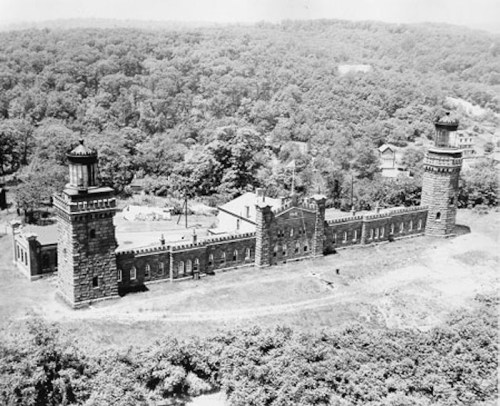 Historic stone building with towers, surrounded by trees and hills, captured in black and white.