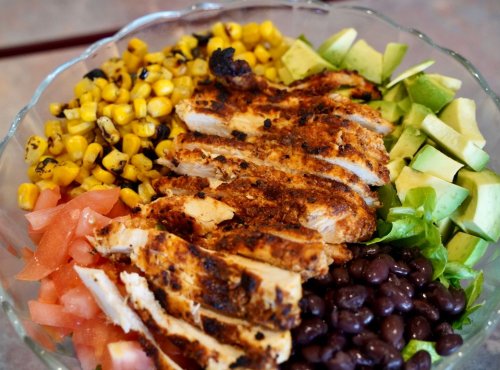 A colorful salad bowl with grilled chicken, corn, black beans, tomatoes, lettuce, and diced green apples.