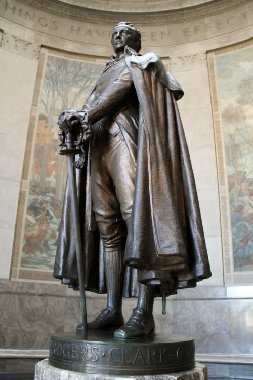 A bronze statue of a man in a cape, holding a sword, stands in a grand hall with murals in the background.