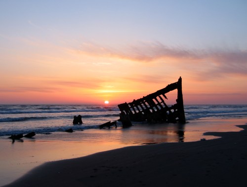 A shipwreck partially submerged on a beach at sunset, with vibrant colors reflecting on the water.