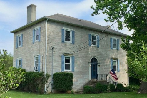 Two-story house with blue shutters, an American flag, and a grassy yard under a clear sky.