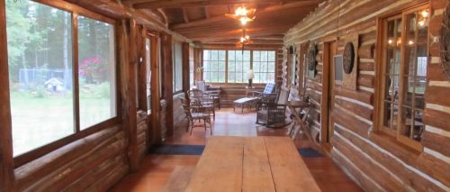 Cozy log cabin interior with wooden beams, large windows, and rustic furniture, creating a warm, inviting atmosphere.