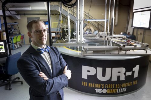 A man in a suit stands confidently in a high-tech lab with a sign reading "PUR-1: The Nation's First All-Digital I&G."