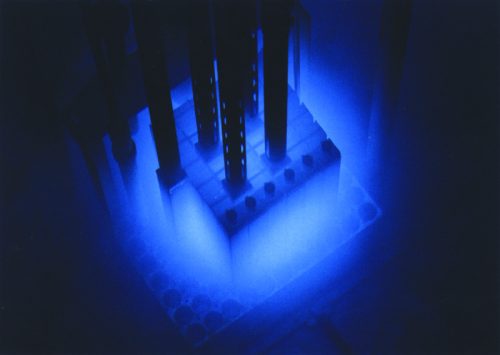 A glowing blue structure with vertical rods, set against a dark background, resembling a scientific or industrial setup.