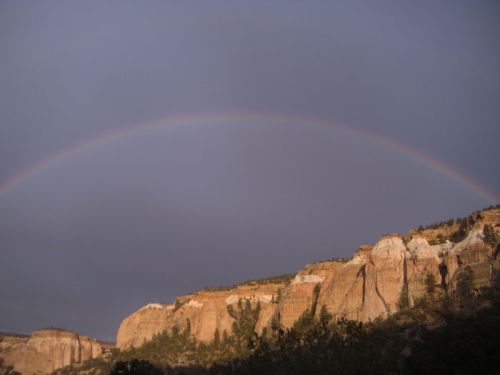 A vibrant rainbow arcs over rugged cliffs under a cloudy sky, showcasing a stunning natural landscape.