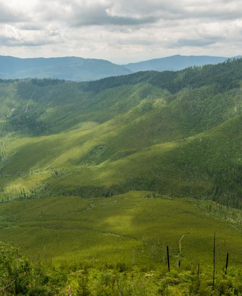 Lush green hills stretch across a mountainous landscape under a cloudy sky, with distant peaks visible in the background.