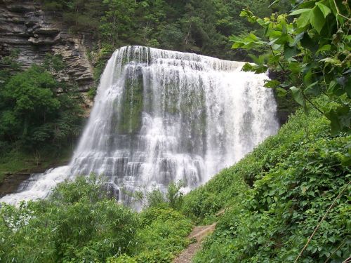A cascading waterfall surrounded by lush greenery and rocky cliffs, creating a serene natural landscape.