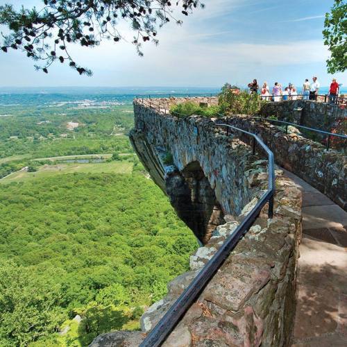 A scenic overlook with visitors, featuring a rocky ledge and lush green valley below under a clear blue sky.