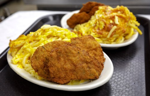 Two plates of comfort food featuring fried chicken and macaroni and cheese on a black tray.