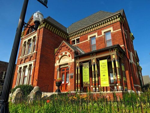 Historic brick building with decorative columns and banners, surrounded by greenery and a clear blue sky.
