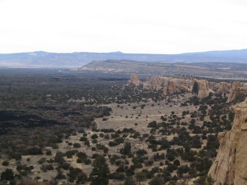 A vast desert landscape with rocky formations and sparse vegetation under a cloudy sky.