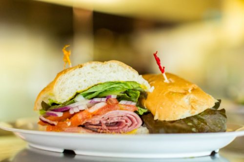 A close-up of a sandwich with layers of ham, lettuce, tomato, and onion, served on a plate with toothpicks.