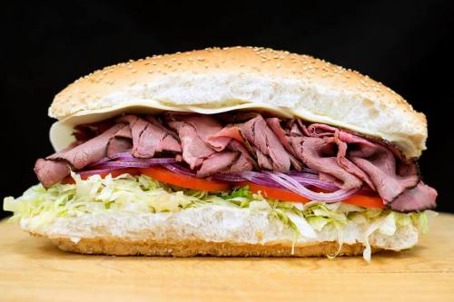 A large sandwich with sesame seed bun, filled with roast beef, lettuce, tomato, and onion.