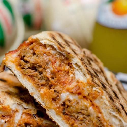 A close-up of a grilled sandwich filled with meat and sauce, showcasing a crispy exterior and savory filling.