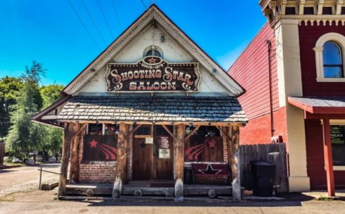 A rustic saloon with a wooden facade, featuring a sign that reads "Shooting Star Saloon" under a clear blue sky.