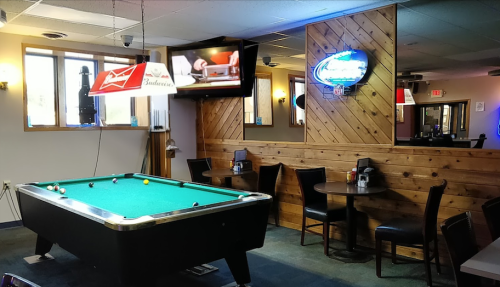 A cozy bar interior featuring a pool table, tables for dining, and a TV on the wall.