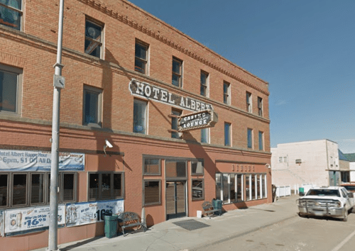Exterior of Hotel Albert, a brick building with a sign for the casino lounge, set in a small town. Clear blue sky above.