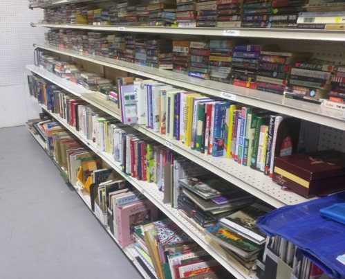 A bookshelf filled with various books and magazines, organized on white shelves in a store.