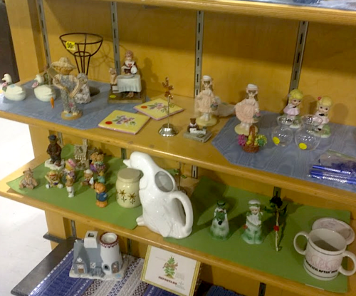 A display of various vintage collectibles, including figurines, dishes, and decorative items on wooden shelves.