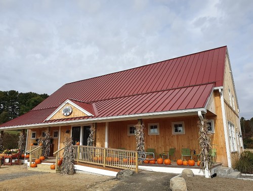 A rustic barn with a red metal roof, surrounded by pumpkins and autumn decor, set against a cloudy sky.