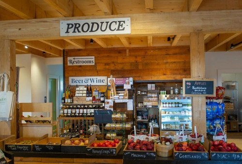 A rustic market display featuring fresh produce, apples, and a selection of beer and wine in a wooden setting.
