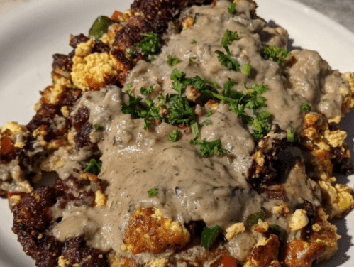 A plate of scrambled eggs topped with a creamy gray sauce and garnished with chopped parsley.