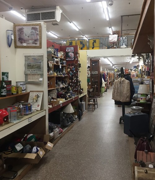 A wide aisle in an antique store filled with various items, including furniture, decor, and collectibles on shelves.
