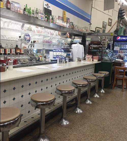 A vintage diner interior featuring a long counter with chrome stools and a variety of drinks displayed behind the bar.