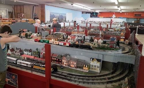 A model train display with intricate buildings and tracks, featuring visitors observing the layout in a spacious room.