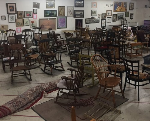 A spacious room filled with various wooden rocking chairs and framed artwork on the walls.