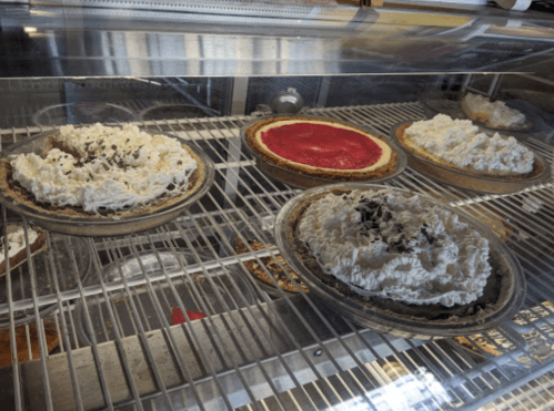 A display case with various pies topped with whipped cream, including chocolate and strawberry varieties.