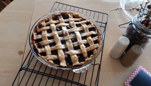 A freshly baked lattice-top pie cooling on a wire rack, with a rustic wooden table and decorative items nearby.