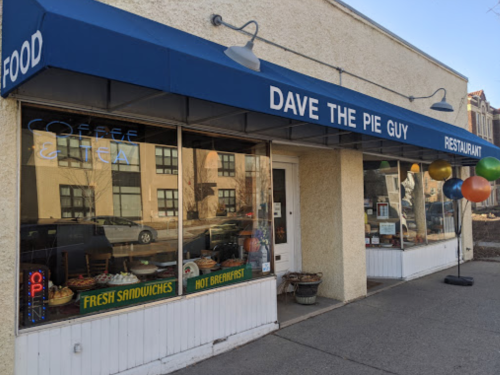 Exterior of "Dave the Pie Guy" restaurant with a blue awning, open sign, and colorful balloons outside.