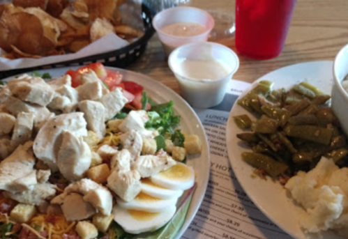 A colorful salad with chicken, eggs, and croutons, alongside green beans, mashed potatoes, and a side of chips.