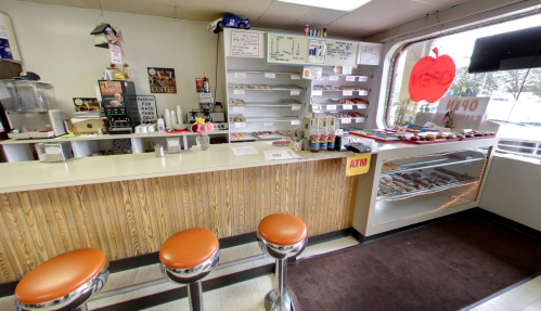 A cozy café interior with a counter, orange stools, a display case of pastries, and a menu on the wall.