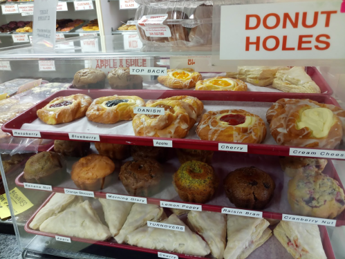 A display case filled with various pastries, including danishes, muffins, and turnovers, labeled "Donut Holes."