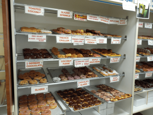 A display case filled with various donuts, including glazed, chocolate, and specialty flavors like red velvet and coconut fudge.