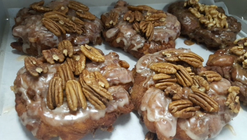 A close-up of glazed pastries topped with pecans and walnuts, arranged in a box.